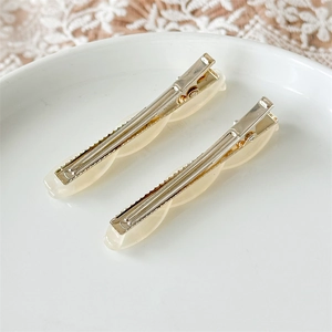 Close-up of two cream-colored wavy acetate hair clips on a white ceramic plate
