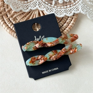 Close-up of twisted acetate hair clips in green and caramel marble texture on display