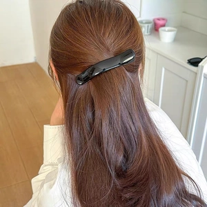 Close-up of a glossy black minimalist curved hair clip holding long brown hair in a half-up style