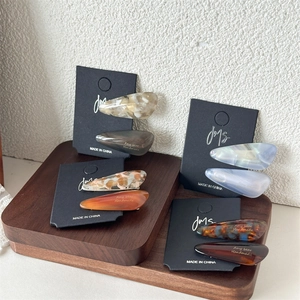 Retro teardrop acetate hair clips set in marble and amber textures on wood stand