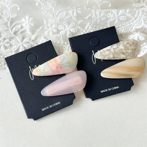 Close-up of four teardrop acetate hair clips with marble texture on black display cards