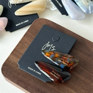 Detailed close-up of acetate water-drop hair clips with amber tortoise pattern on wood tray