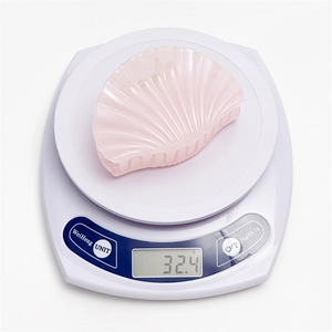 Détail d'une pince à cheveux coquillage rose pesant 32,4g sur une balance blanche
