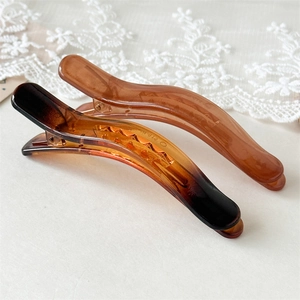 Detail view of large curved resin hair clips in amber and brown with a glossy jelly finish