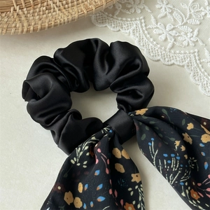 Detail of elegant black satin hair scrunchie with colorful floral print long ribbons
