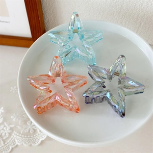 Three hollow star-shaped hair claws in blue, orange, and purple on a white ceramic tray