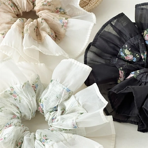 Detailed view of floral hair scrunchies with chiffon edges in cream, white, and black colors