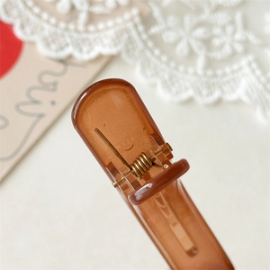 Macro detail of brown jelly hair clip showing golden metal spring and grip mechanism