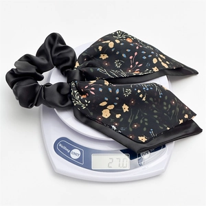 Black double-layer satin scrunchie with floral bow being weighed at 27.0g for quality