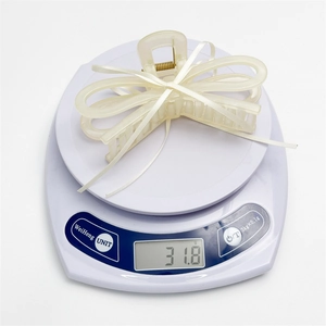 Détail d'une pince à cheveux avec nœud crème pesant 31,8 g sur une balance