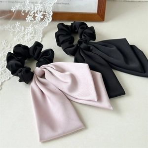 Detail of satin scrunchies with long bows in black and soft pink on a white lace background