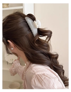 Détail d'une grande pince à cheveux marbrée dans une coiffure demi-haute de couleur crème
