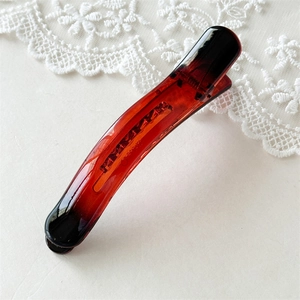 Detail of a large amber-colored curved hair clip with jelly texture and black gradient ends