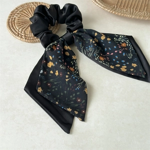 Detail of a black floral satin ribbon scrunchie with colorful flower patterns on a textured surface