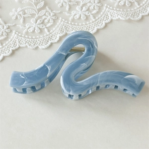 Gros plan d'une grande pince à cheveux bleue marbrée au design ondulé sur dentelle blanche