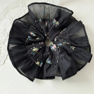 Detail of a black floral organza scrunchie with ruffled edges and lightweight texture