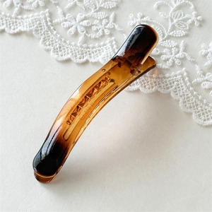 Detail of amber tortoiseshell duckbill hair clip with metal spring on lace background