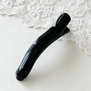 Close-up of a glossy black curved hair clip with anti-slip teeth and a piano lacquer finish