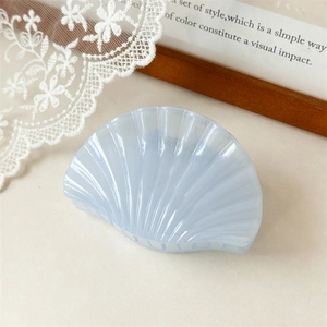 Détail d'une pince à cheveux nacrée bleu clair en forme de coquillage avec texture à rayures