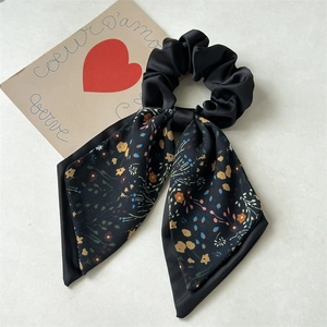 Detailed view of black satin bow scrunchie with colorful floral print and elegant ribbons
