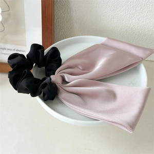 Detail showing elegant satin bow scrunchie in pink and black on a ceramic tray