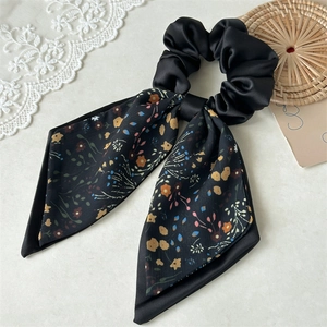 Macro detail of a black satin bow scrunchie with floral pattern on white background