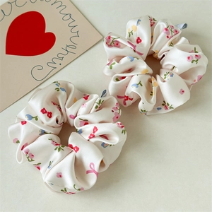 Detailopname van twee satijnen scrunchies met roze bloemen en strikken op beige stof
