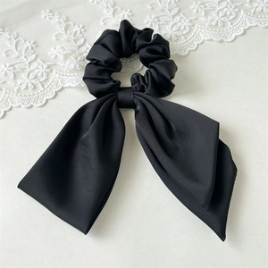 Detail view of a black satin bow scrunchie with long ribbons on a white background