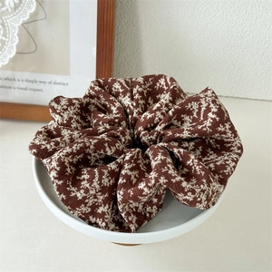 Close-up of floral fabric hair scrunchie in dark brown with white print in a ceramic dish