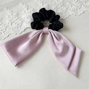 Detail of satin scrunchie with pink bow and black pleated fabric with silk texture
