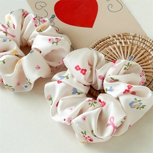 Detail van bloemen zijden scrunchie met rode bloemetjes op beige satijnen stof