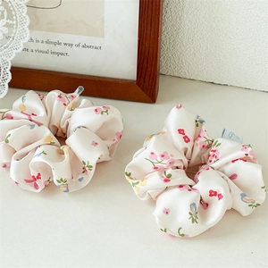 Detailweergave van twee bloemige zijden scrunchies met roze patronen op beige satijn
