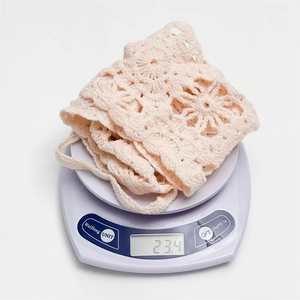 Detail showing the lightweight 23.4g cream crochet headscarf on a digital scale