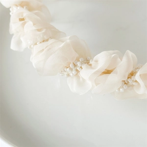Detail of pleated beige mesh headband featuring delicate white pearl bead accents