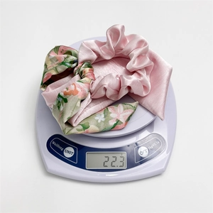 Close-up showing a light pink floral satin scrunchie set weighing 22.3 grams on a scale