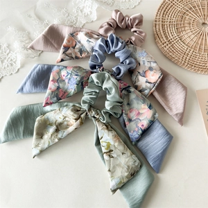 Three satin bow scrunchies with floral and solid colors on a minimalist background