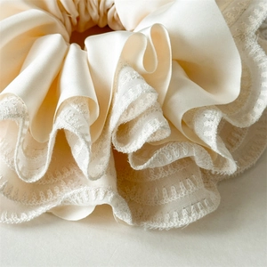 Close-up of cream lace and satin scrunchie showing delicate pleated layers and texture