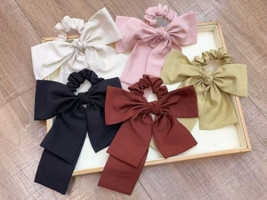 Detailed set of five colorful satin bow scrunchies with long ribbons on a wooden tray