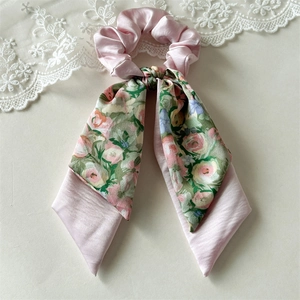 Detail of pink satin scrunchie with floral rose pattern ribbon on soft beige background