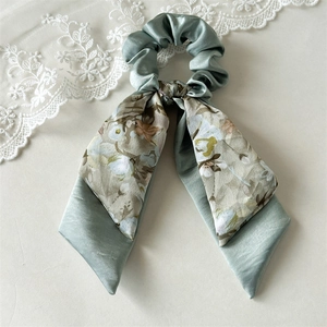 Detail of sage green satin scrunchie with floral bow streamers on a lace background