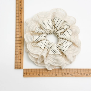Close-up of dual-layer hair scrunchie with beige lace edges and black polka dots pattern