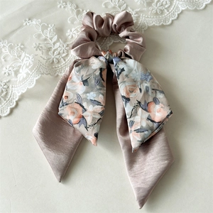 Close-up of champagne satin hair scrunchie with long bow and vintage floral pattern