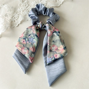 Close-up of grey blue satin scrunchie with floral pattern bow and long ribbons