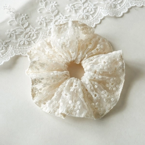 Détail d'un chouchou en dentelle blanche avec broderie florale et texture plissée