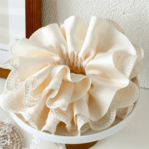 Close-up detail of oversized lace and satin layered scrunchie in elegant beige