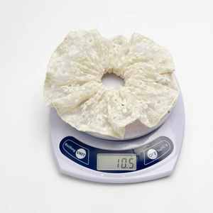 Détail d'un chouchou en dentelle blanche avec broderie marguerite pesant 10,5 g sur balance