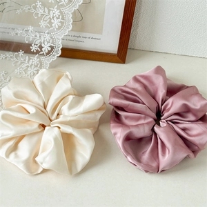 Close-up of premium satin hair scrunchies in cream and dusty pink with silky texture