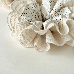 Close-up of elegant off-white lace and polka dot layered scrunchie with embroidery edges