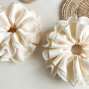 Macro detail of creamy satin hair scrunchie featuring elegant lace edges and soft folds