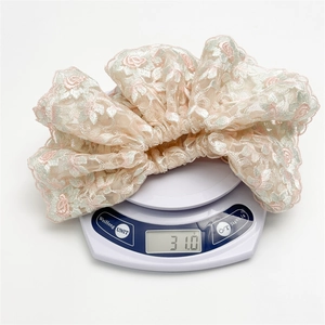 Chouchou en dentelle florale avec broderie rose et bords ondulés sur balance
